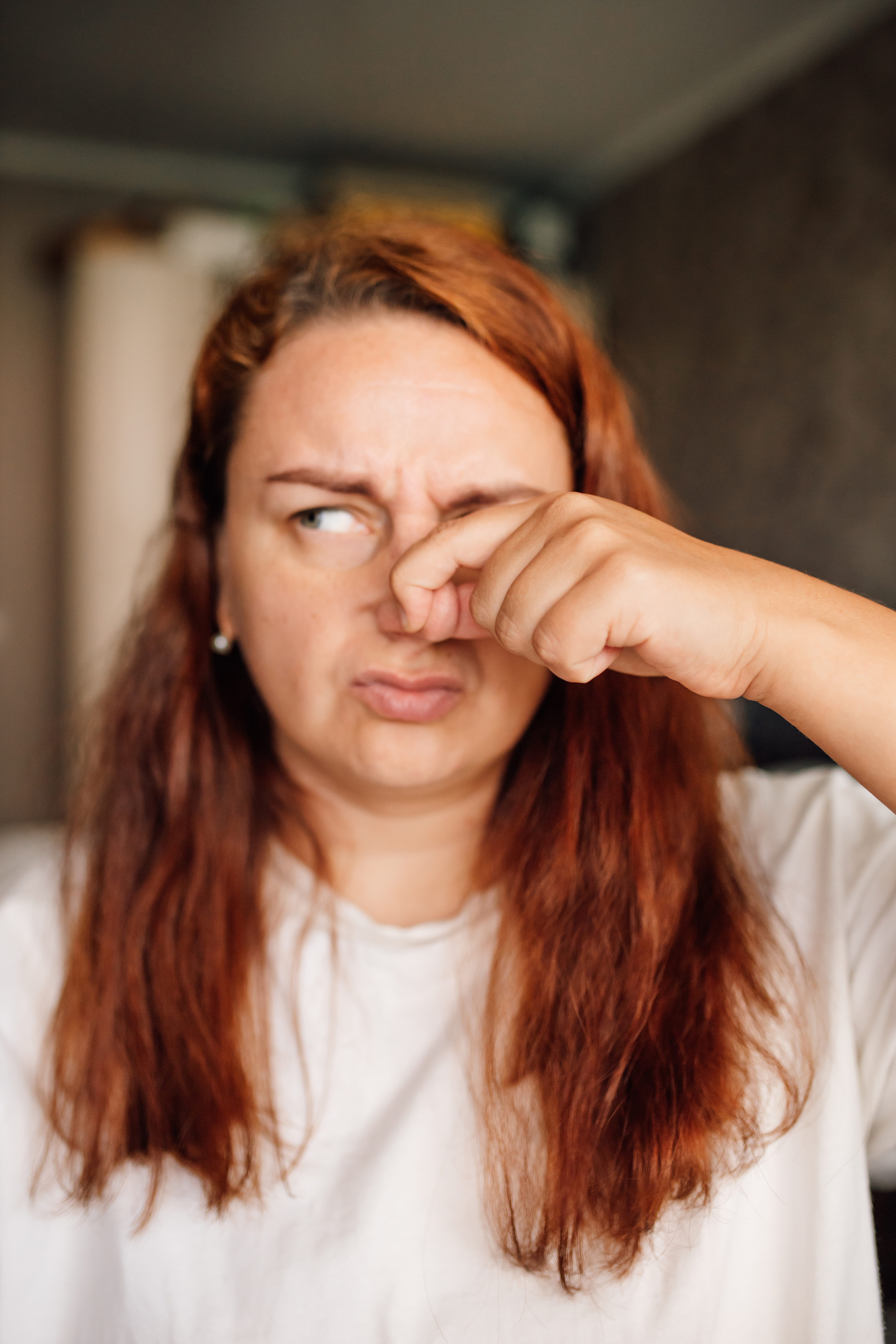 Person pinching nose, scrunching face in reaction to a bad smell, wearing a casual shirt indoors