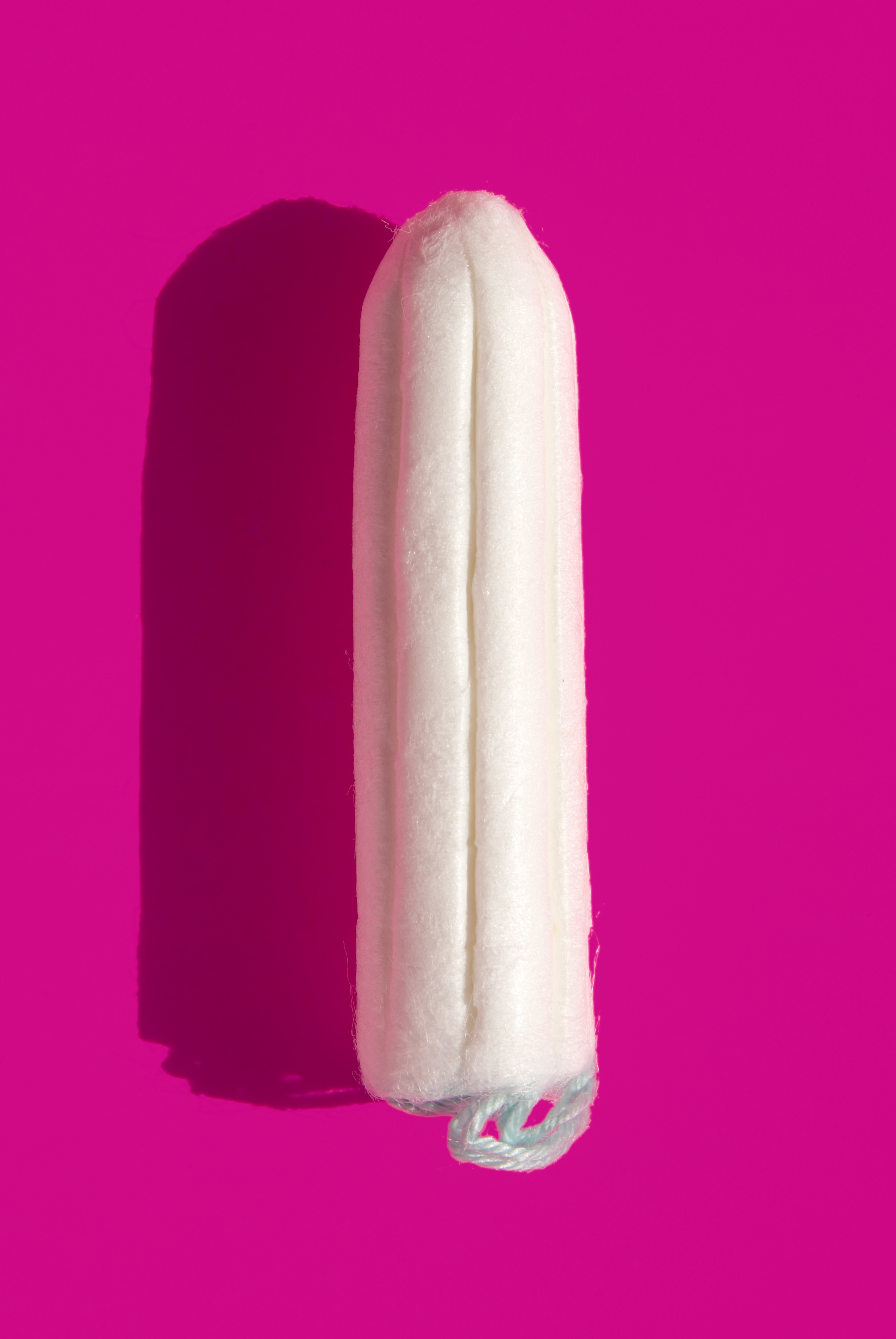 A tampon on a pink background, casting a shadow to the left
