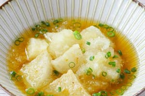 焼きおにぎりがしょっぱいスープに浮かび、細かく切ったネギが散りばめられた料理。