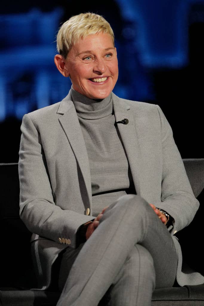 Person in a gray suit and turtleneck top, sitting on a chair and smiling during an interview