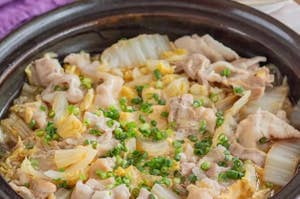 土鍋に入った豚肉とキャベツの料理、青ネギが散りばめられた食欲をそそる熱々の一品。