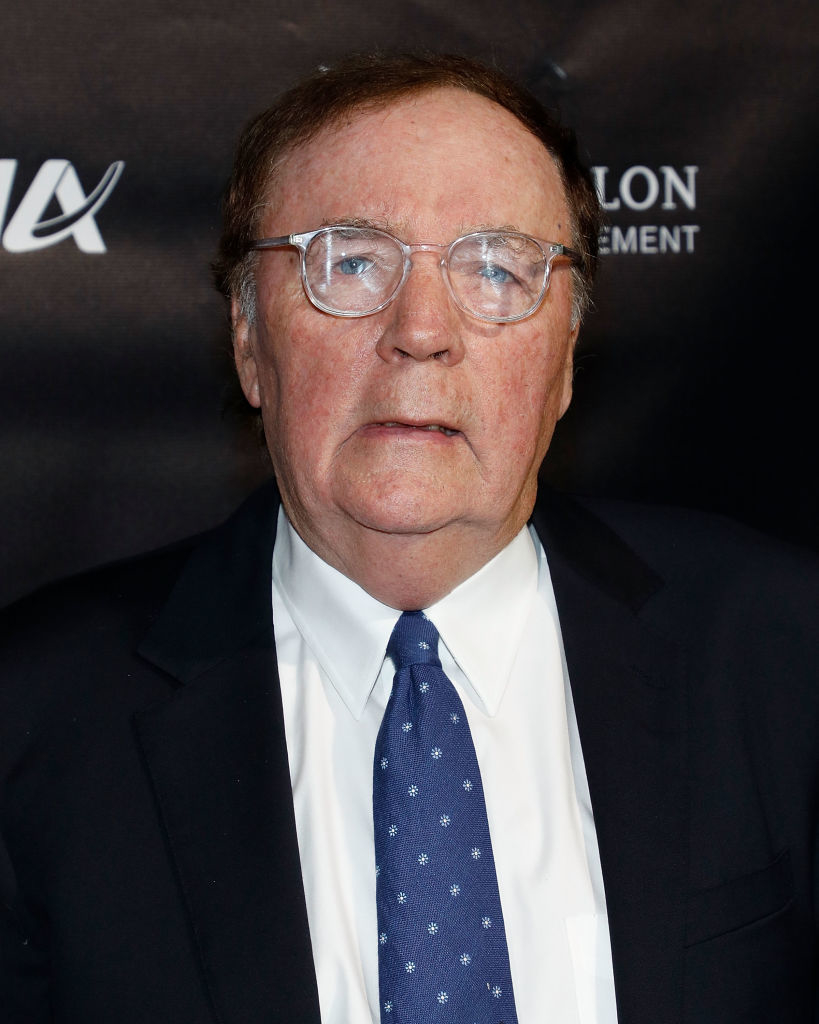 A person in a suit and tie on a red carpet, wearing glasses