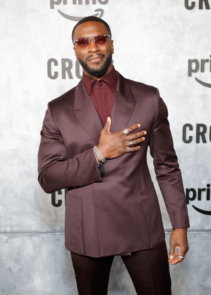 Man wearing a stylish suit with sunglasses, posing on a red carpet event backdrop