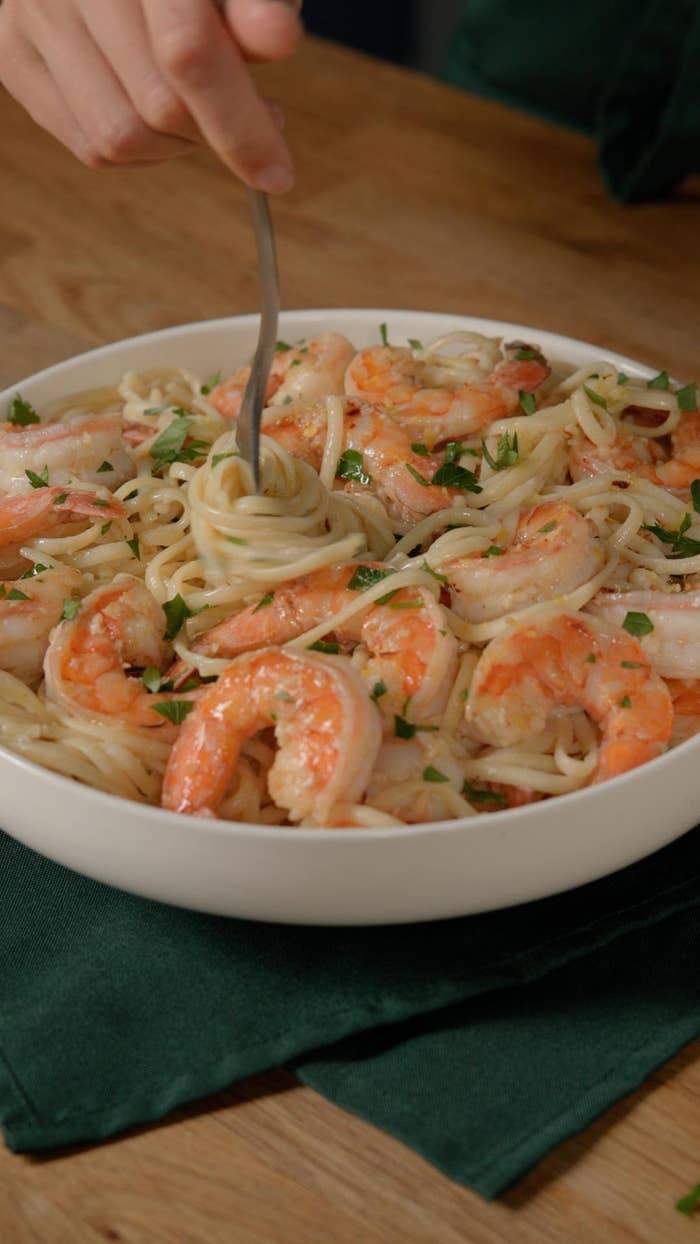 Shrimp linguine pasta with herbs being twirled on a fork in a white bowl on a wooden table