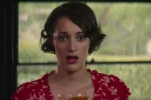 Person with short hair, wearing a floral-patterned dress, looks surprised while holding a drink in front of them