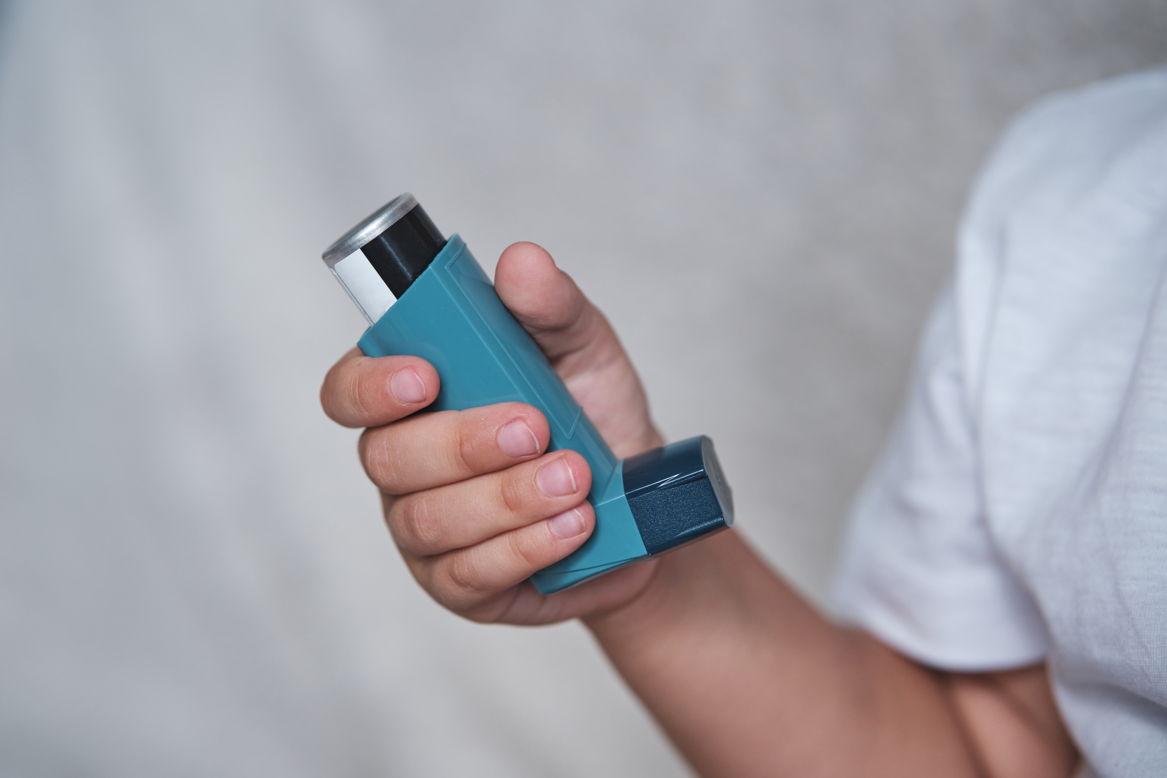 A person&#x27;s hand holding an asthma inhaler, prepared to use it