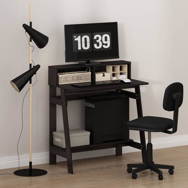 Compact home office setup with a small desk, computer, black swivel chair, and modern floor lamp