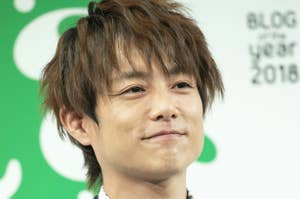 男性がスーツと蝶ネクタイを着用し、笑顔でマイクを持っている。