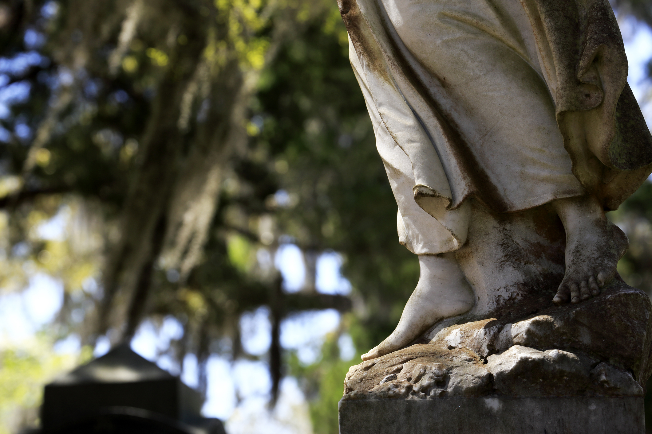 石造りの人物の足元が写っている彫刻。背景に木々が見える。