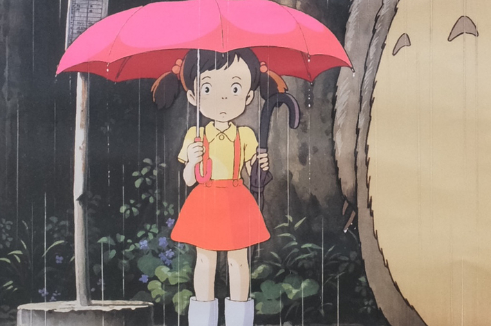 女の子が赤い傘をさし、森の生物と雨の中に立っている。アニメ映画の一場面。