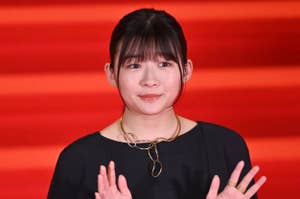 有名人が赤いカーペットでシンプルな黒のドレスを着て立っている。