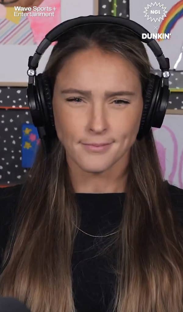 Kylie Kelce wearing headphones, looking focused, with a polka dot wall and colorful art in the background