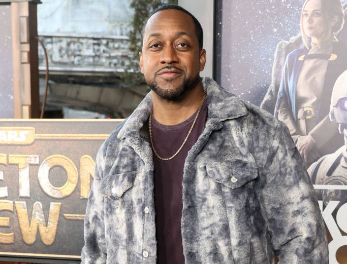 Person in a textured jacket poses at a movie premiere, standing in front of promotional posters