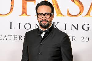Lin-Manuel Miranda in formal attire with glasses on a red carpet for "The Lion King" event signage