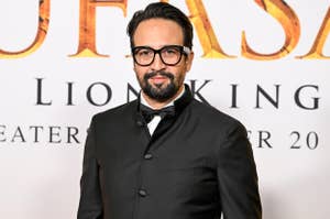 Lin-Manuel Miranda in formal attire with glasses on a red carpet for "The Lion King" event signage
