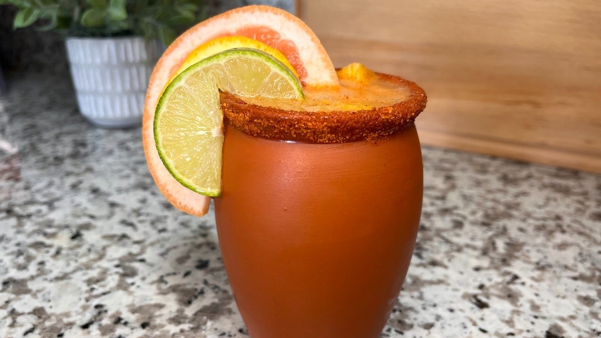 A refreshing drink in a glass with a chili-rimmed edge, garnished with lime and grapefruit slices