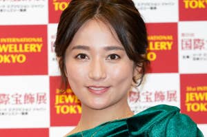 女性がジュエリー展示会の背景で、エレガントな緑のドレスを着ています。