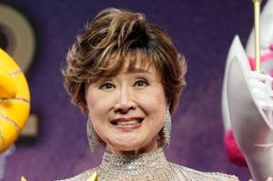 有名人が舞台上で、豪華なビーズ装飾の赤いドレスを着て、金色の仮面を持つ姿。