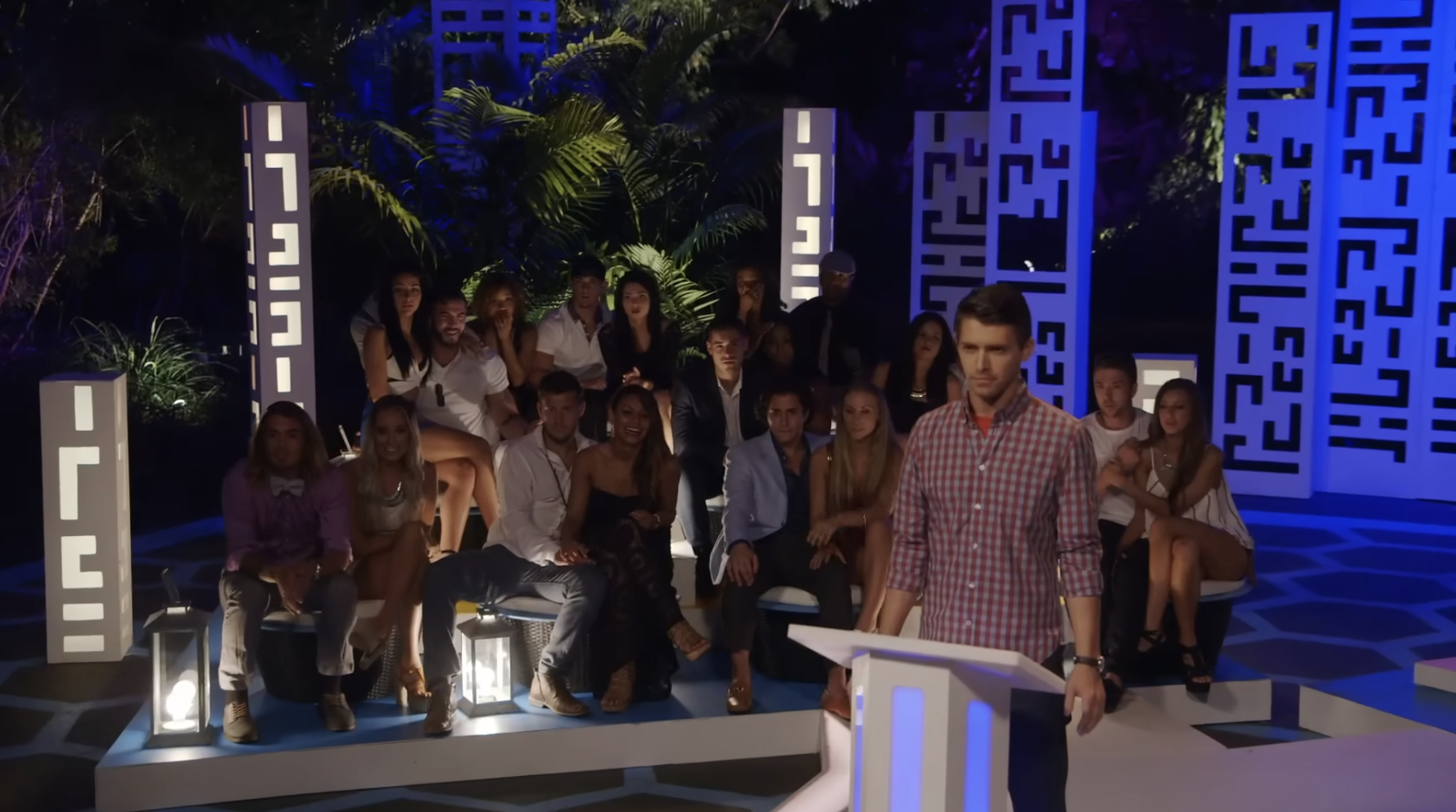 The group of singles sit at the matching ceremony outdoors, with host Ryan Devlin standing at a podium awaiting the reveal of matches