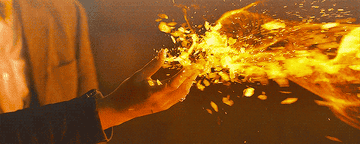 Una mano sostiene fragmentos llameantes en movimiento, creando un efecto dinámico de fuego y luz