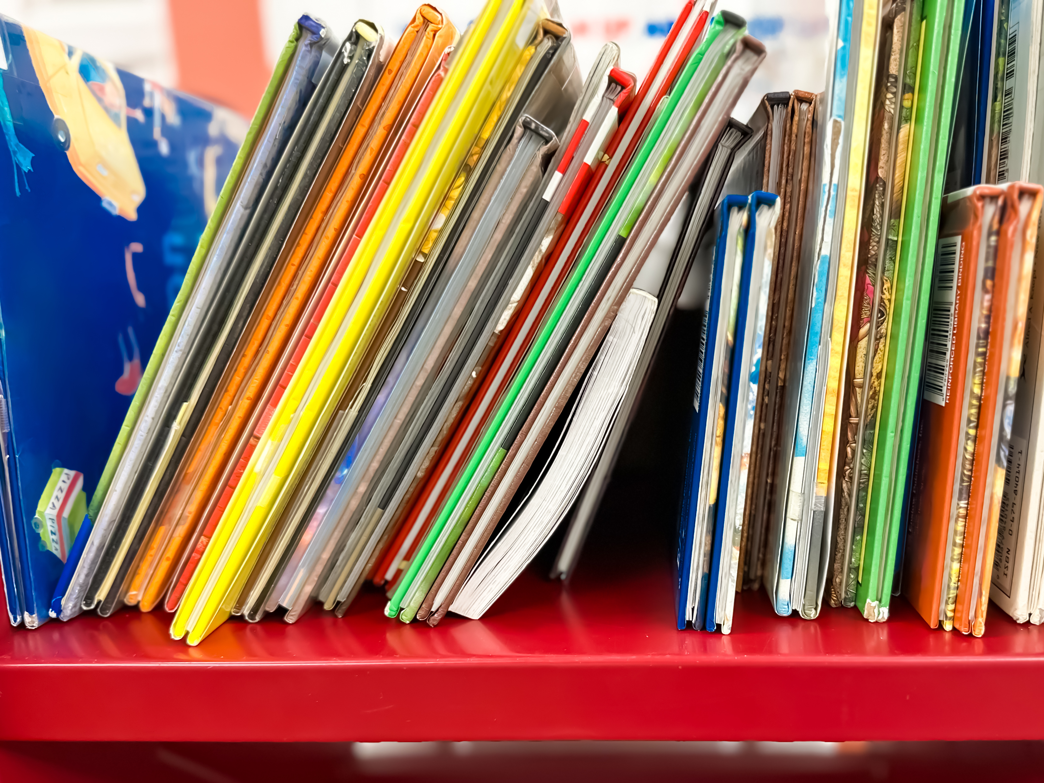 Close-up of assorted children&#x27;s books standing upright on a red shelf.