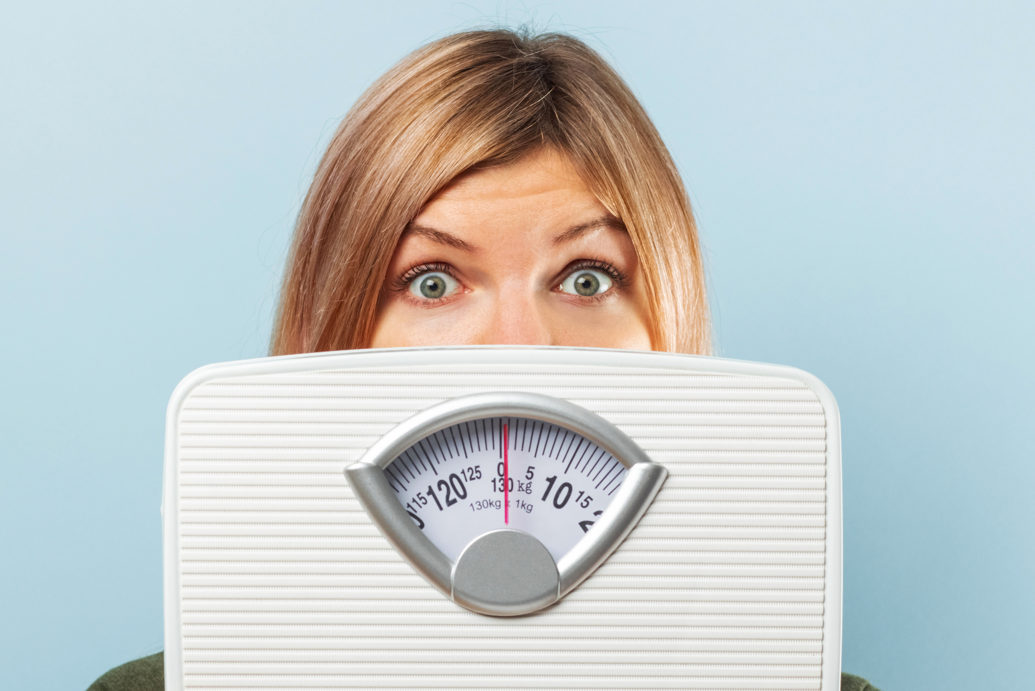 Woman looking over bathroom scale, face partially hidden, with a surprised expression.