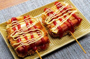 長方形の皿に盛られた2本のホットドッグ、ケチャップとマスタードがかかっている。