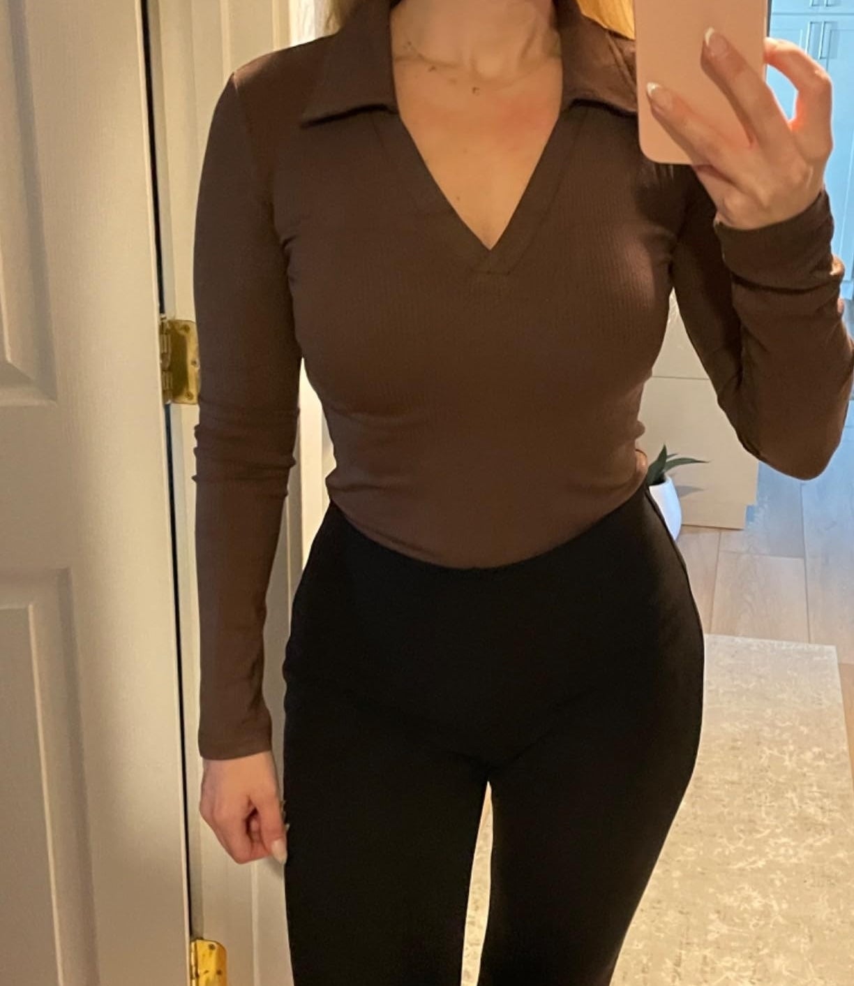 a reviewer taking a mirror selfie, wearing a fitted long-sleeve brown top with a V-neck and high-waisted pants