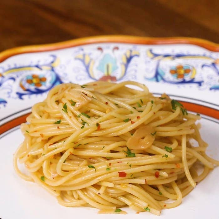 A plate of spaghetti aglio e olio garnished with parsley and red pepper flakes, served on a decorative plate