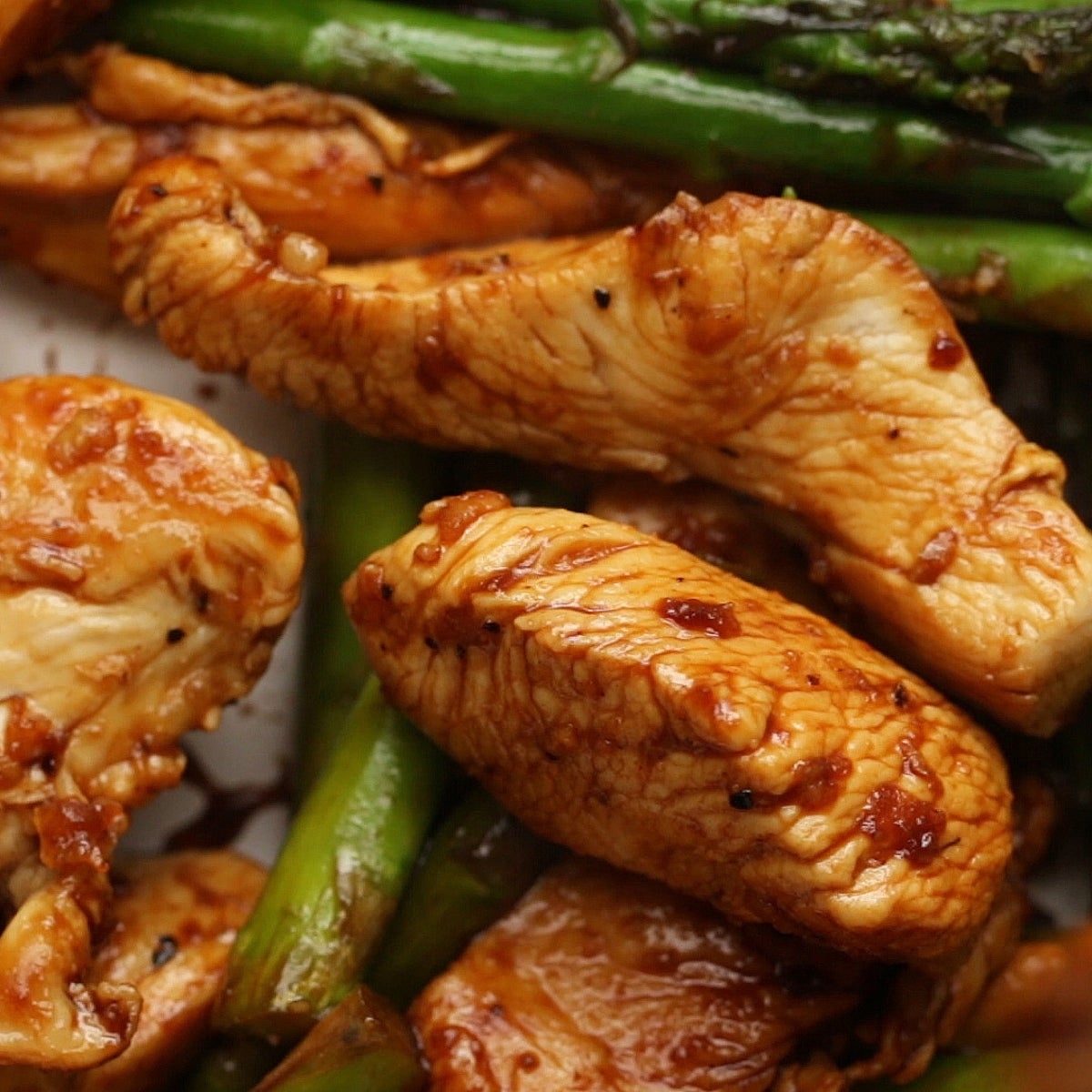 Close-up of stir-fried chicken pieces with asparagus, glazed in a savory sauce