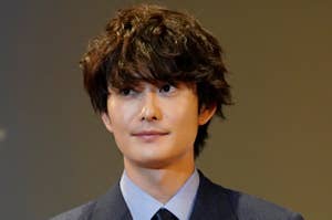 男性がダブルブレストのスーツを着て、赤いリボンを付けている。