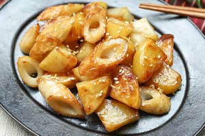 ごまがかかった揚げちくわとじゃがいもの料理が黒い皿に盛られています。背景に箸と植物が見えます。