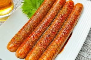 お皿に並べられた4本の焼きソーセージ。付け合わせに緑の葉と飲み物がある。