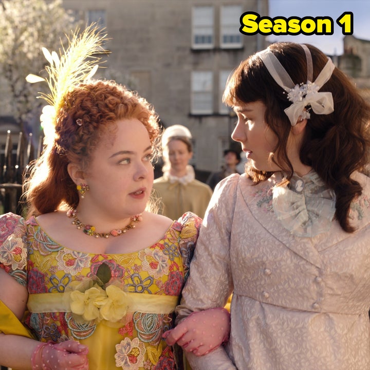 Two women in Regency-era dresses walk arm in arm, engaging in conversation. Both dresses have intricate patterns and elegant accessories