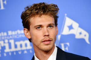 Austin Butler in a formal suit at a film festival event, standing against a backdrop featuring a film-related logo