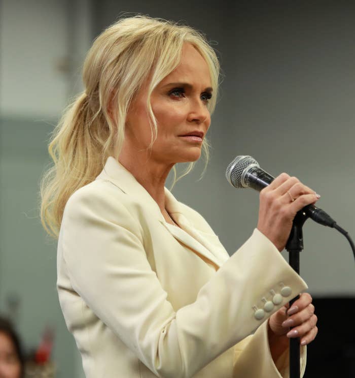Kristin Chenoweth speaking into a microphone with a serious expression on her face