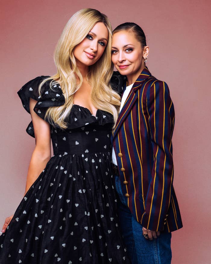 Two women posing together; one in a ruffled dress with heart patterns, the other in a striped blazer