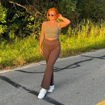 Person walking connected a paved road, wearing a fitted top, flared pants, and sneakers, surrounded by trees and earthy greenery