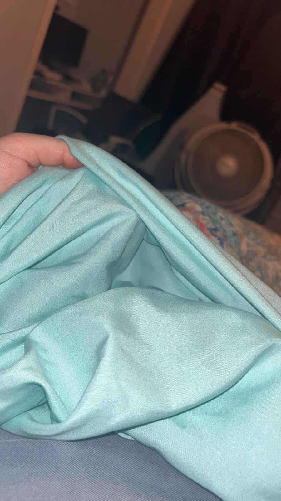 Hand holding soft, folded fabric, shown indoors adjacent   a fan