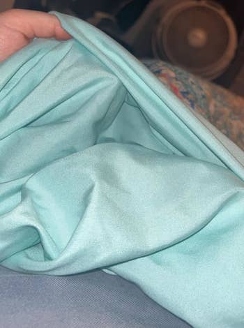 Hand holding soft, folded fabric, shown indoors adjacent a fan