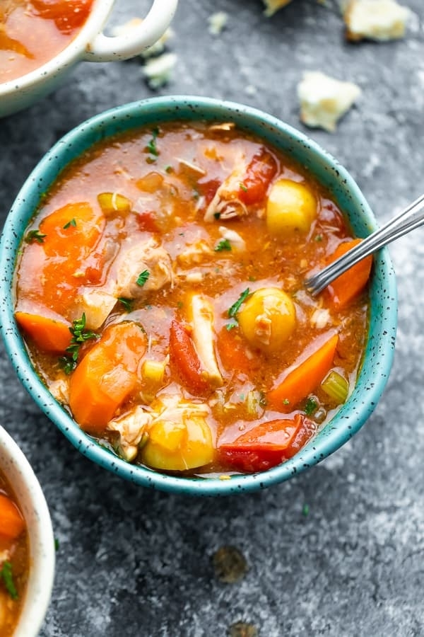 Bowl of hearty vegetable soup with carrots, potatoes, and herbs, sitting on a textured surface