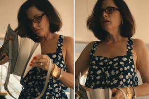 Person in patterned dress holding a purse, wearing glasses and jewelry, in a casual setting