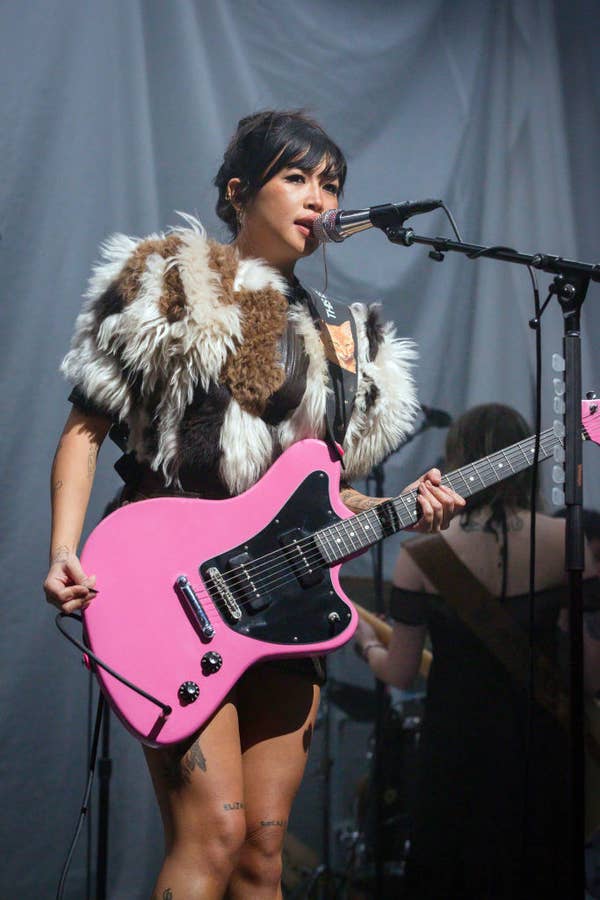 Beabadoobee performs on stage with a guitar, wearing a fur-inspired top, singing into a microphone
