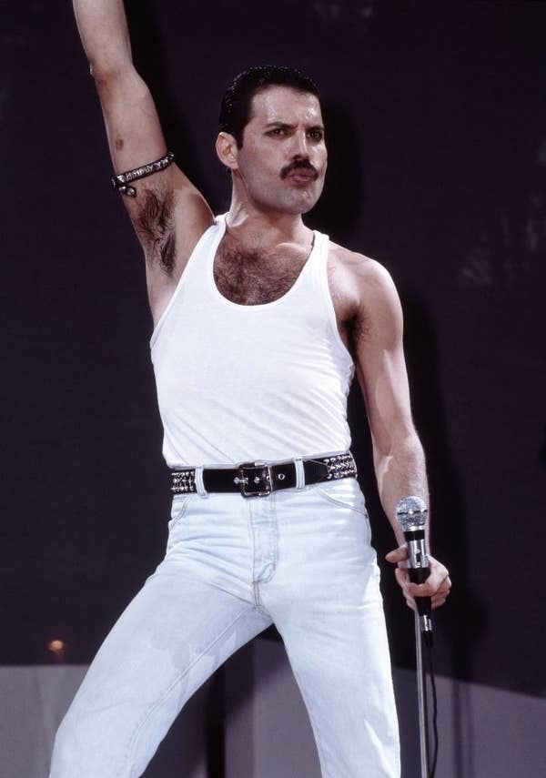 Freddie in a tank top and jeans performs energetically on stage, holding a microphone with an arm raised