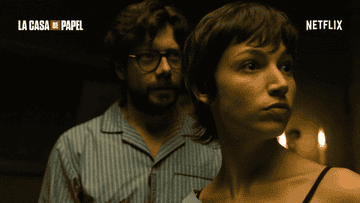 Two characters from the TV show &quot;La Casa de Papel&quot; look serious in a dimly lit room. The man wears glasses and striped pajamas