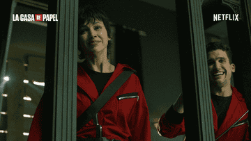 Two people in red costumes with black accents, smiling and looking through mirrors, from &quot;La Casa de Papel.&quot; Text reads &quot;Netflix&quot; and &quot;La Casa de Papel.&quot;