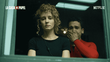 Two characters from &quot;La Casa de Papel&quot; look solemnly out of a window. One covers their mouth with their hand. Netflix branding visible