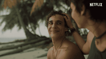 Person on a tropical beach smiles warmly while another person gently ruffles their hair, palm trees in the background. Netflix logo visible
