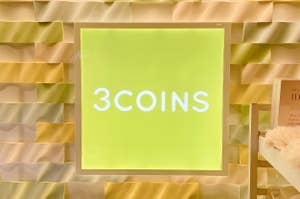 壁に「3COINS」と書かれた看板。背景は波模様のデザイン。
