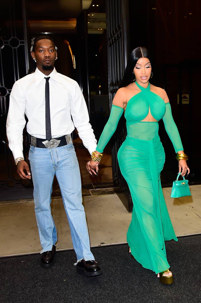 Offset and Cardi B holding hands, one wearing a white shirt and jeans, the other in a stylish, fitted green dress, walking on a street